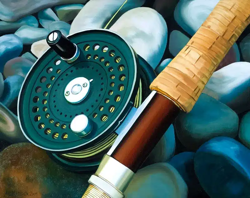 Close-up of a green fishing reel with a brown wooden rod handle resting on smooth blue and gray stones.